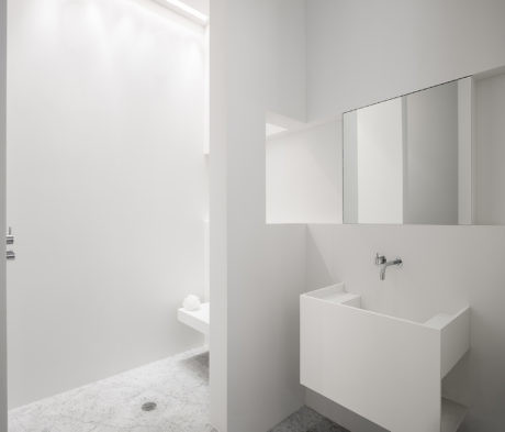 Minimalist white bathroom with geometric sink and terrazzo flooring.