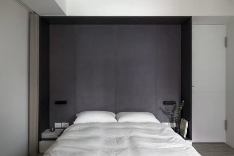 Modern bedroom with a large gray headboard, white bedding, and minimalist decor.