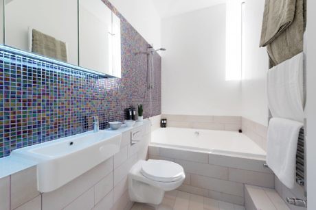 Modern bathroom with a mosaic tile wall, white fixtures, and towels hanging.
