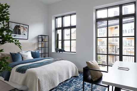 Modern bedroom with large windows, blue and white bedding, and a small desk area