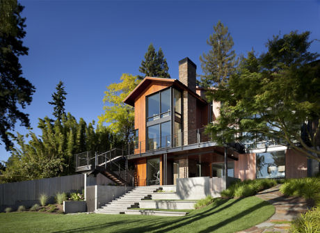 Modern house with large windows, brick chimney, and surrounded by trees.