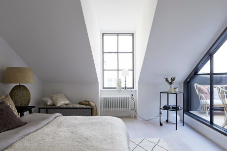 Minimalist attic bedroom with sloped ceiling, large window, and neutral tones.