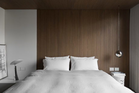 Modern bedroom with white bedding and wooden wall paneling.
