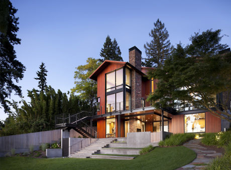 Modern two-story house with large windows and warm lighting at dusk.