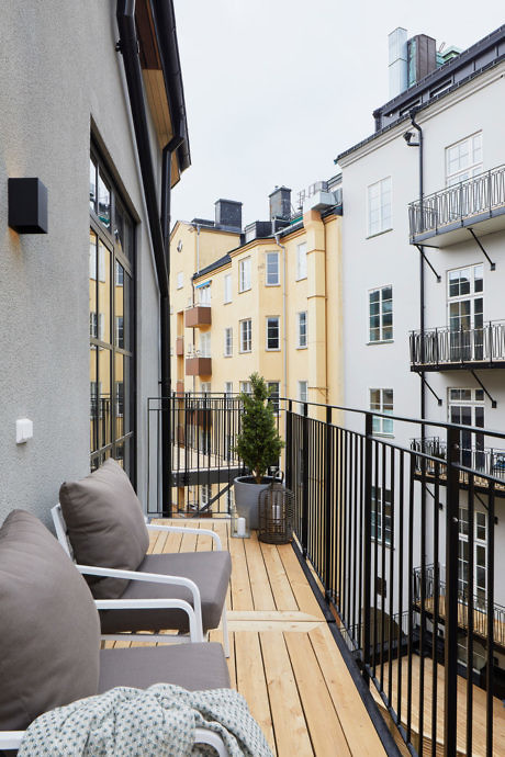 Narrow balcony with wooden flooring and outdoor seating overlooking other buildings.