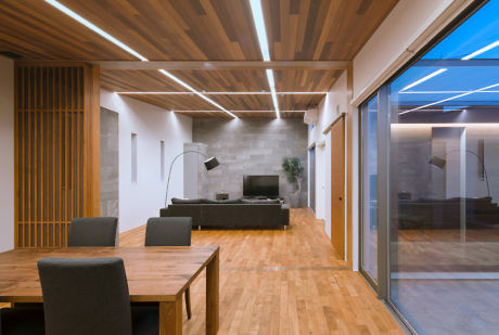 Modern living room with wooden floors, ceiling, and furniture, lit by strip lighting