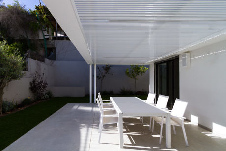 Modern outdoor patio with a white dining table and chairs under a pergola.