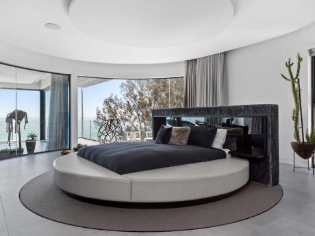 Modern bedroom with round bed, panoramic windows, and ocean view.