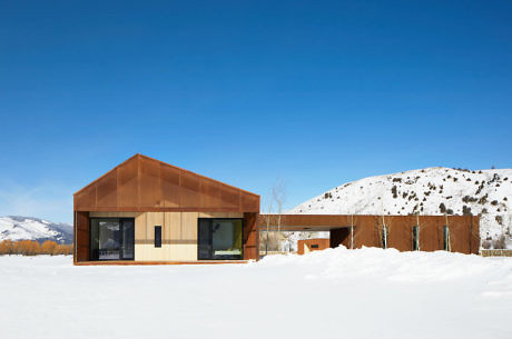 Modern house with a rusted metal roof in a snowy landscape.