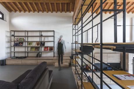 Contemporary room with exposed wooden beams, metal shelving, and blurred person.