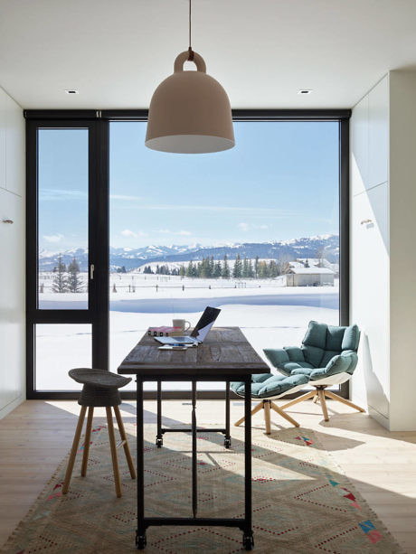 Modern home office with a desk and chair facing a window overlooking snowy landscape.