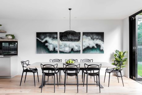 Modern dining room with black chairs, large triptych wall art, and pendant