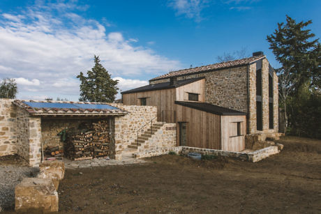 Rustic stone house with modern wooden extension under a clear sky.