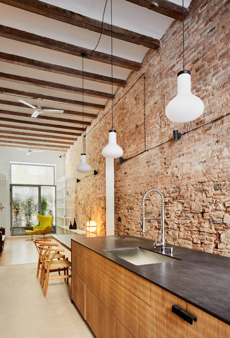 Modern kitchen with exposed brick wall, wooden ceiling beams, and hanging lights.