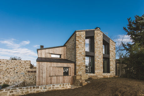 Contemporary stone house with large windows and contrasting wood paneling.