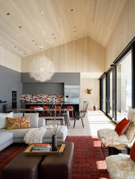 Modern cozy living room with wooden ceiling, stylish furniture, and kitchen area.