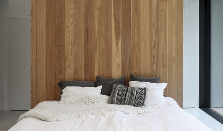 Modern bedroom with a wooden wall behind a bed with white and grey pillows.