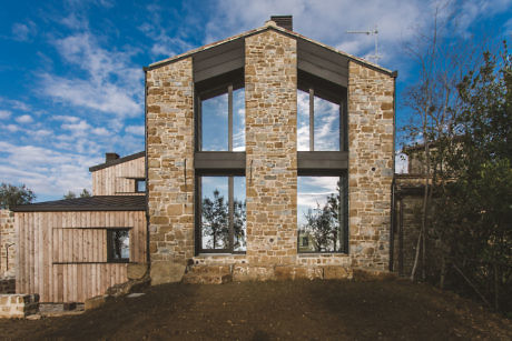 Modern stone house with large windows and a clear blue sky.