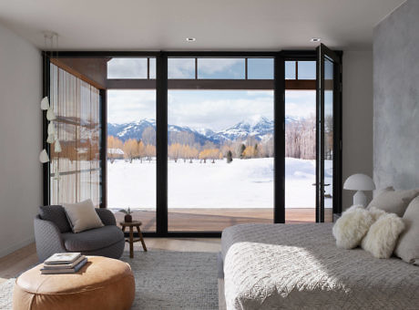 Modern bedroom with large windows showcasing snowy mountain view.