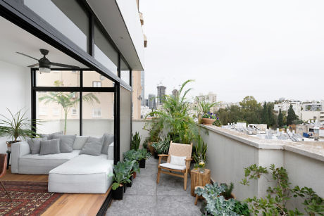 Urban balcony with plants and comfy seating overlooking a cityscape.