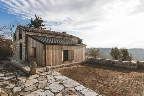 Rustic stone and wood house with a patio overlooking a hilly landscape.