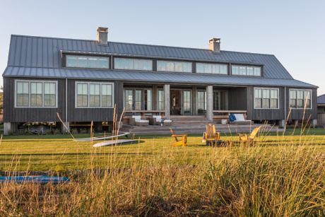Modern two-story house with large windows and outdoor seating.