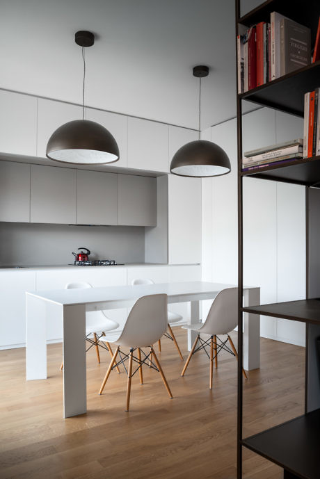 Modern kitchen with white furniture, pendant lights, and a bookshelf.