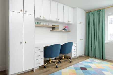 Minimalist home office with white cabinets, blue chairs, and colorful rug.