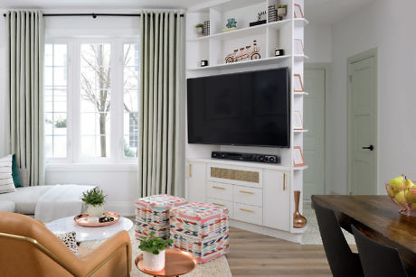 Modern living room with TV, white shelving, and colorful ottomans.