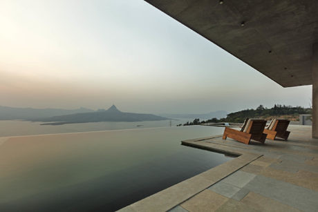 Infinity pool with lounge chairs overlooking a serene lake at sunset.