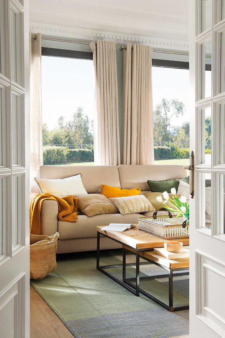 Sunny living room with a beige sofa, green accents, and open French doors