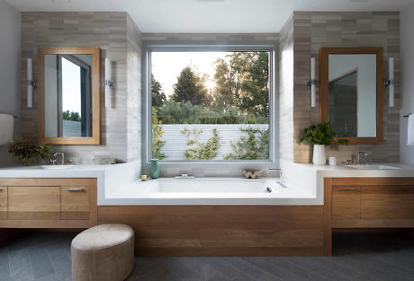 Modern bathroom with wooden cabinets and a large window above the bathtub.