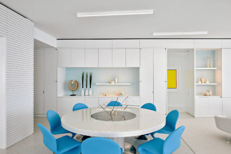 Minimalist white dining room with bold blue chairs and sleek shelving.