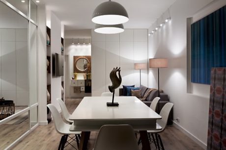 Modern dining room with white table, pendant light, and mirrored wall.