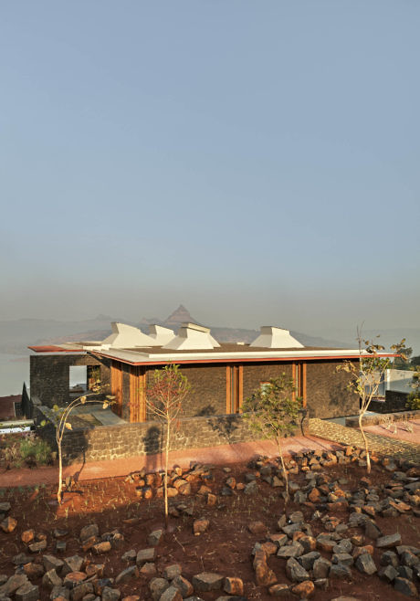 Modern house with angular roofs on rocky terrain overlooking a body of water.