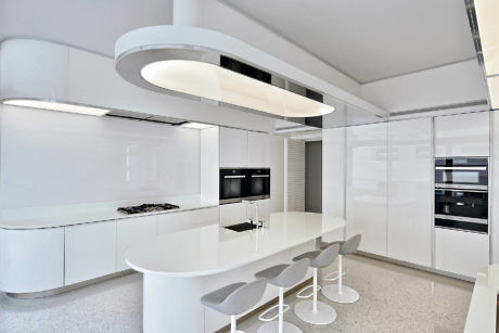 Sleek white kitchen with curved island and overhead lighting.