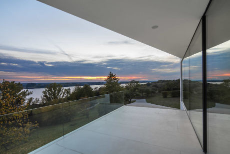 Modern terrace with glass balustrade overlooking a lake at sunset.