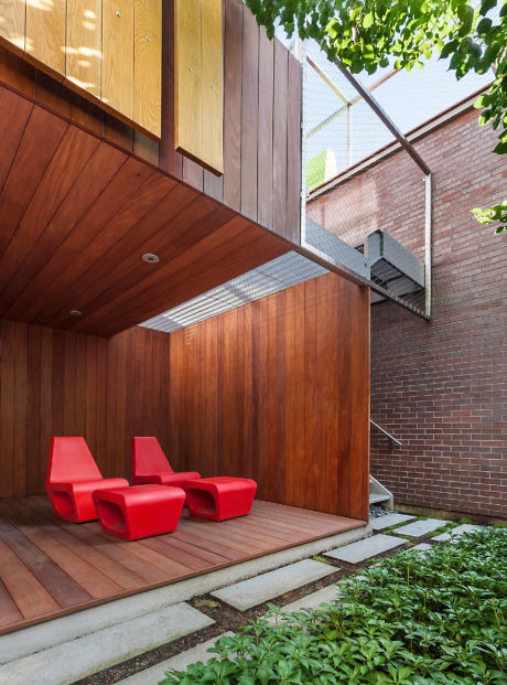Contemporary wooden patio with red chairs and lush greenery.