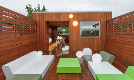 Modern outdoor patio with wooden walls, white furniture, and green accents.