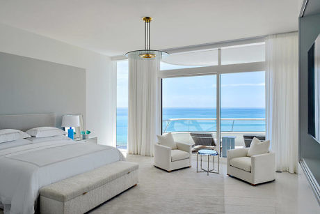 Modern bedroom with ocean view through floor-to-ceiling windows.