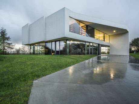 Modern house with large glass windows and a white facade at dusk.