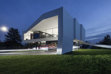 Modern house with large glass windows at dusk, featuring light trails from a passing car