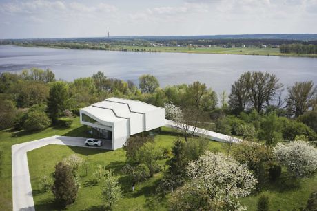 Contemporary white cubic house by the lakeside with a lush green lawn.