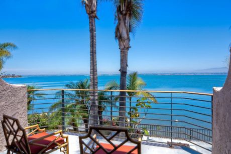 Coastal balcony with seating and ocean view, flanked by palm trees.