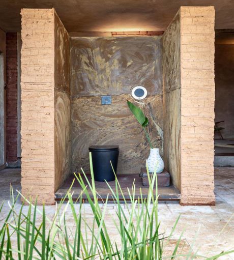 Rustic niche with textured walls, modern mirror and green plant accents.