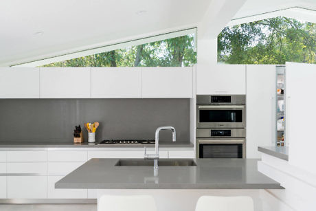 Sleek white kitchen with built-in appliances and gray backsplash.