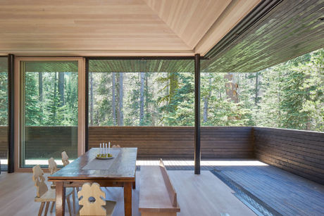 Modern wooden dining area with large windows overlooking a forest.