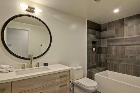 Contemporary bathroom with circular mirror and wood-toned tiles.