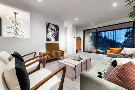 Modern living room with sofa, chairs, and wall art, overlooking a balcony.