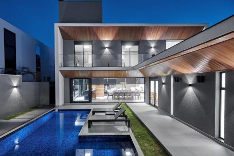 Modern house with illuminated interior, pool, and wooden accents at dusk.